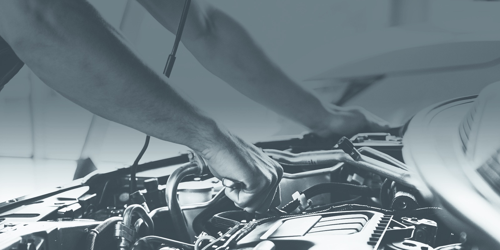 Mechanic's hands working under the open hood of a car, ratchet in hand